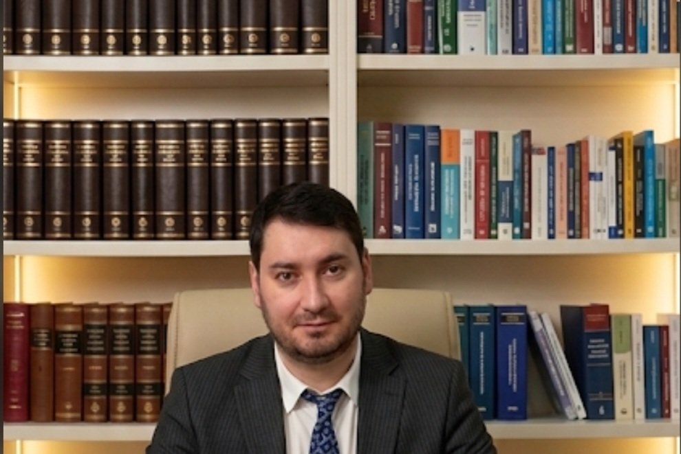 Elşad Səfixanov iş masasında, kitab rəfi qarşısında